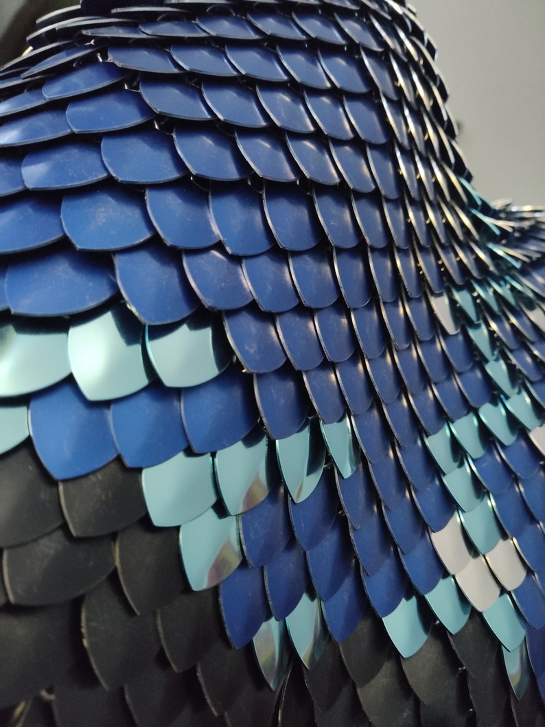 May include: Close-up of a blue and black chainmail armour made of interlocking metal scales. The scales are arranged in a pattern that resembles fish scales.