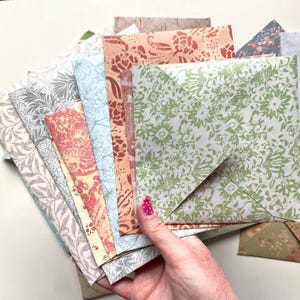 Peut inclure: Une collection d'enveloppes en papier à motifs de différentes couleurs et de différents motifs. Les enveloppes présentent des motifs floraux, botaniques et abstraits dans des tons de vert, de rose, de bleu et de beige. Les enveloppes sont tenues dans une main.