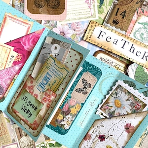 May include: A selection of handmade paper ephemera, including tags, tickets, and journal cards. The items feature butterfly and floral designs, with text that reads "It's your story" and "Fea TheR". The colour palette includes shades of blue, pink, and brown.