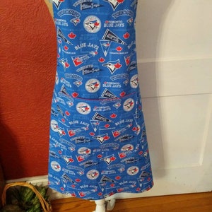 Peut inclure: Un tablier bleu avec un motif imprimé répétitif du logo des Toronto Blue Jays, du nom de l'équipe et de feuilles d'érable rouges. Le tablier comprend une poche avant et des bretelles, affichant les graphismes de l'équipe en blanc, rouge et bleu marine.