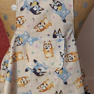 GIRLS BLUEY APRON --- ages  3-7 -- girls flared skirt with lined pocket with pink ties at neck and waist, trim on bib