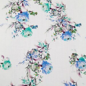 May include: White fabric with a repeating floral pattern. The design features clusters of blue, teal, and purple flowers with green foliage. The flowers are in various stages of bloom, creating a delicate and elegant look.