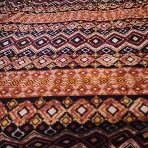 May include: A fabric with a repeating geometric pattern in shades of brown, red, yellow, and white. The pattern is made up of diamonds, squares, and zigzags.