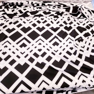 May include: Black and white geometric patterned fabric with a diamond pattern. The fabric is folded and has a slight sheen.