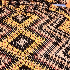 May include: Black fabric with a geometric pattern in shades of yellow, orange, red, and white.