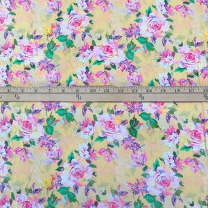 May include: Floral fabric with a yellow background and a pattern of pink and white roses, purple flowers, and green leaves. A ruler with inch measurements is across the bottom of the image.