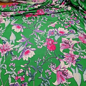 May include: Green fabric with a vibrant floral pattern. The design features large pink and white flowers, purple accents, and green foliage. The fabric is likely used for clothing or home decor.