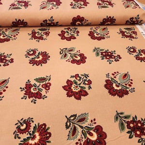 May include: A roll of fabric featuring a repeating floral pattern. The flowers are a deep burgundy color with green leaves and accents, set against a light peach background. The fabric is likely cotton or a similar material, suitable for quilting or crafting projects.