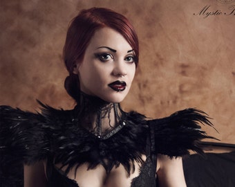 May include: A woman in a black corset, lace bra, and feathered shoulder piece. The image has a gothic aesthetic, with dark makeup and the text "Mystic Thread" in the upper right corner.