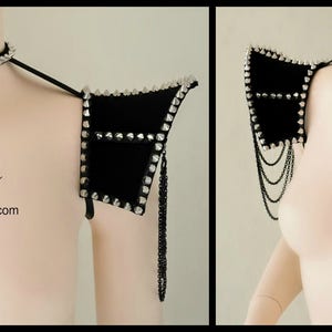 May include: A pair of black velvet shoulder pads with silver studs and chains. The shoulder pads are worn on a mannequin with a silver choker necklace.