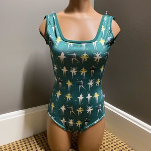 Op de afbeelding: Een groene maillot met een patroon van dansende ballerina's in geel, roze en blauw. De maillot heeft een vierkante halslijn en is mouwloos.