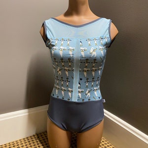 Op de afbeelding: Een blauwe maillot met een wit en groen patroon van dansers. De maillot heeft een ronde hals en een mesh-paneel aan de voorkant. De maillot heeft een donkerblauwe onderkant.