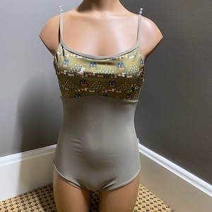 Op de afbeelding: Een groene maillot met een gepatroneerd bovenstuk met een herhalend ontwerp van gestileerde bomen en vogels. De maillot heeft een ronde hals en dunne bandjes.