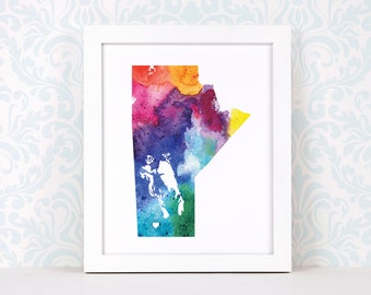 May include: A watercolor painting of the outline of the Canadian province of Manitoba in a rainbow of colors. The painting is framed in a white frame and is displayed on a white shelf.