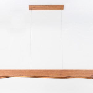 May include: A wooden pendant light fixture with a natural wood finish. The light fixture is suspended from the ceiling by two cords. The wood has a natural, organic shape.
