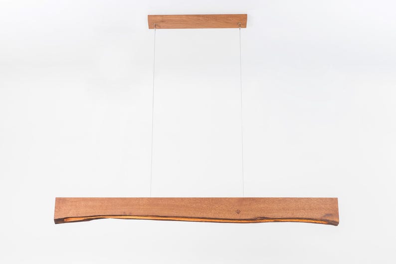 May include: A wooden pendant light fixture with a natural wood finish. The light fixture is suspended from the ceiling by two cords. The wood has a natural, organic shape.
