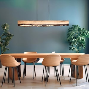 May include: A wooden dining table with four chairs. The table is made of light wood and has a natural finish. The chairs are also made of wood and have black metal legs. The table is set in a room with a teal blue wall and a large window. A wooden light fixture hangs above the table.