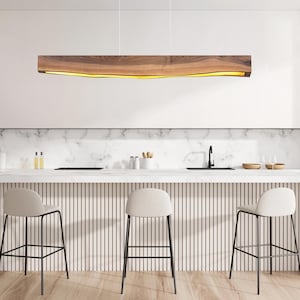 May include: A modern kitchen with a white countertop and three white bar stools. A wooden light fixture hangs above the countertop.