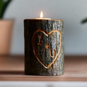 May include: A wooden candle holder shaped like a tree trunk with a heart carved into it. The heart has the words "I + U" carved inside. A small white candle is burning inside the holder.