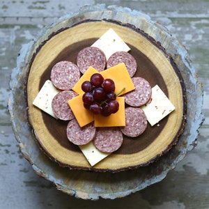 May include: A wooden serving board with a variety of snacks, including salami, cheese, and grapes. The board is made of natural wood and has a rustic look.
