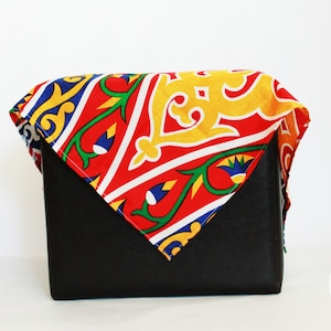 May include: A black box wrapped in a red, yellow, blue and green patterned fabric with geometric designs. The fabric has a white border.