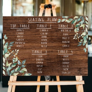 May include: A wooden seating plan with a rustic brown background and green foliage accents. The chart lists the names of guests for a wedding reception, organised by table number. The text "SEATING PLAN" is at the top of the chart.
