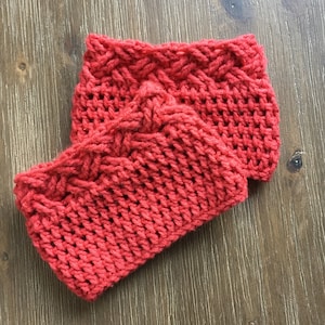 May include: Two red knitted cosy cup sleeves. The sleeves are made with a cable knit pattern.