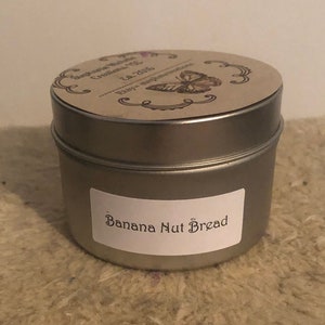 May include: A silver metal candle tin with a brown paper label that says "Banana Nut Bread".