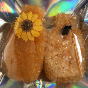 May include: Two amber-colored wax melts, one shaped like a bottle and the other with a sunflower on top.
