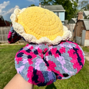 May include: A crocheted stuffed animal shaped like a turtle. The shell is yellow with a white crocheted border. The body is a mix of pink, purple, and gray.