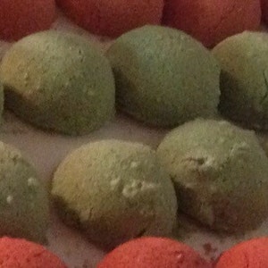 May include: A close-up of a tray of small, round, green and red candies. The candies are arranged in a grid pattern.