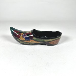 May include: A small, black ceramic shoe with colorful floral designs. The shoe is a traditional Dutch design, known as a "klomp".