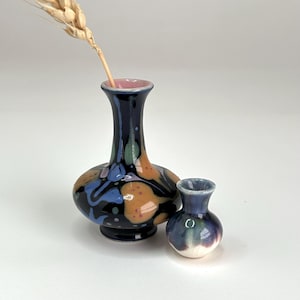 May include: Two ceramic vases, one larger than the other. The larger vase has a blue, black, and orange abstract design. The smaller vase is a solid blue color. Both vases have a white glaze.