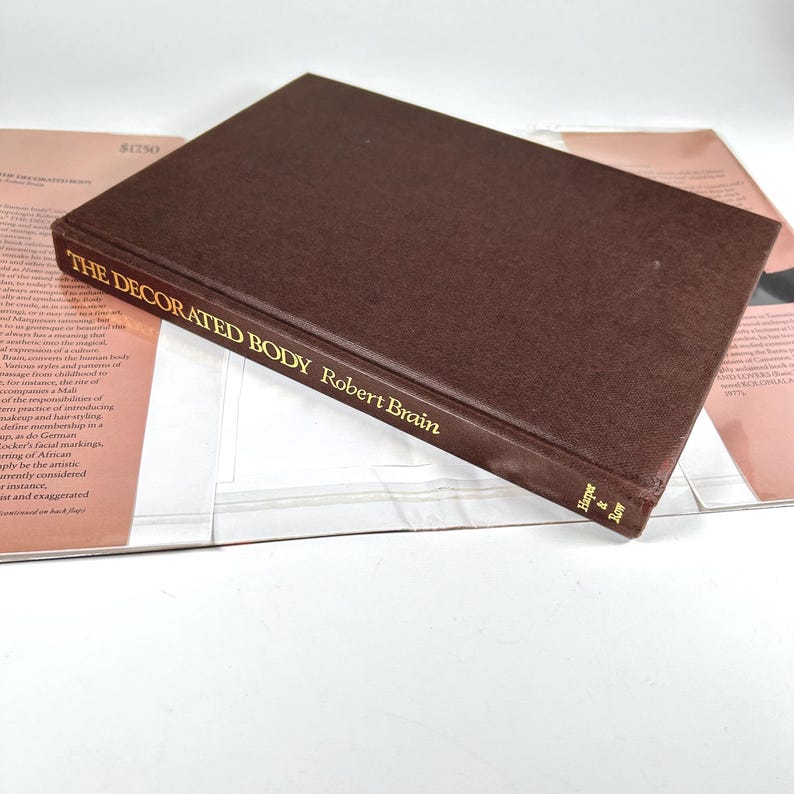 May include: A brown hardcover book titled "The Decorated Body" by Robert Brain. The book is closed and lying on top of a white surface.