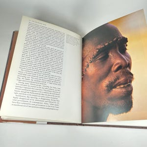 May include: Close-up portrait of a person with intricate scarification markings on their face. The markings are raised and create a textured pattern across the forehead, cheeks, and chin. The person's eyes are closed, and their mouth is slightly open, revealing a hint of a smile.