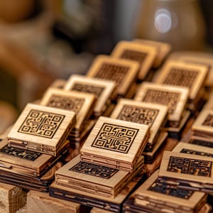 May include: A stack of wooden coasters featuring a laser-etched QR code design. The coasters are made from light brown wood and have a natural finish.