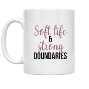 May include: White ceramic mug with the text "Soft life & strong boundaries" in a mix of rose gold and black fonts. The mug has a curved handle and a glossy finish.