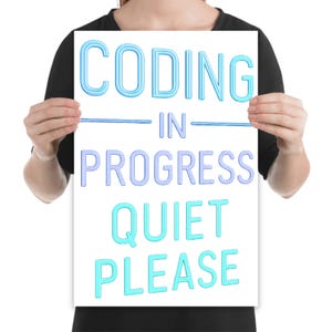 May include: A white poster with the words "CODING IN PROGRESS QUIET PLEASE" in blue and light blue lettering. The poster is being held up by a person.