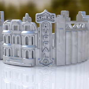 May include: A silver 3D printed model of the Buffalo skyline, featuring the Shea's Buffalo Theatre, a historic building, and grain silos. The model is a decorative piece for a home or office.