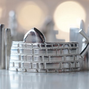 Puede incluir: Un anillo de plata con un diseño detallado de un edificio con una cúpula y un molino de viento. El anillo está hecho de metal y tiene un acabado brillante.