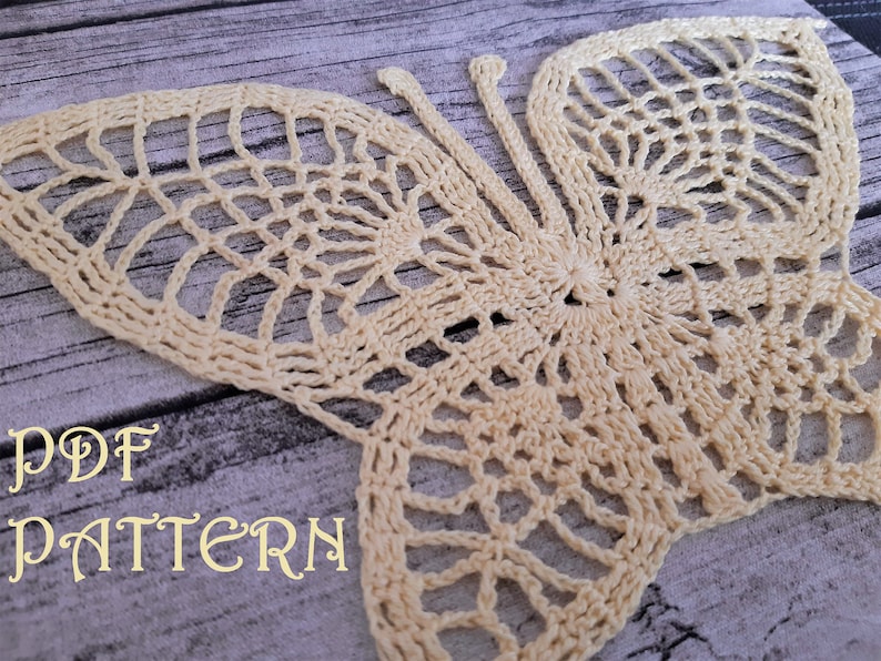 Puede incluir: Un patr&oacute;n de mariposa tejido a crochet en color crema. El patr&oacute;n est&aacute; sobre un fondo de madera con el texto "PDF PATTERN" en color crema.