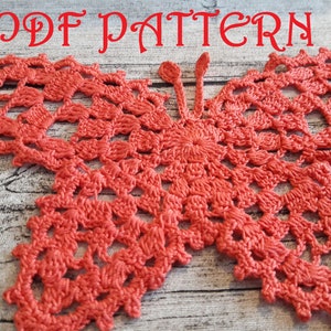 May include: A crochet butterfly pattern in a bright coral color. The pattern is intricate and detailed, with a delicate lace design. The butterfly is shown on a wooden background.