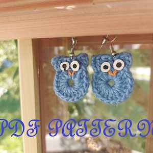 May include: A pair of blue crocheted owl earrings with white eyes and orange beaks. The earrings are hanging from silver hooks. The text "PDF PATTERN" is written in blue cursive letters at the bottom of the image.