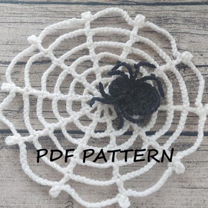 May include: A white crocheted spider web with a black crocheted spider in the center. The text "PDF PATTERN" is written below the spider web.