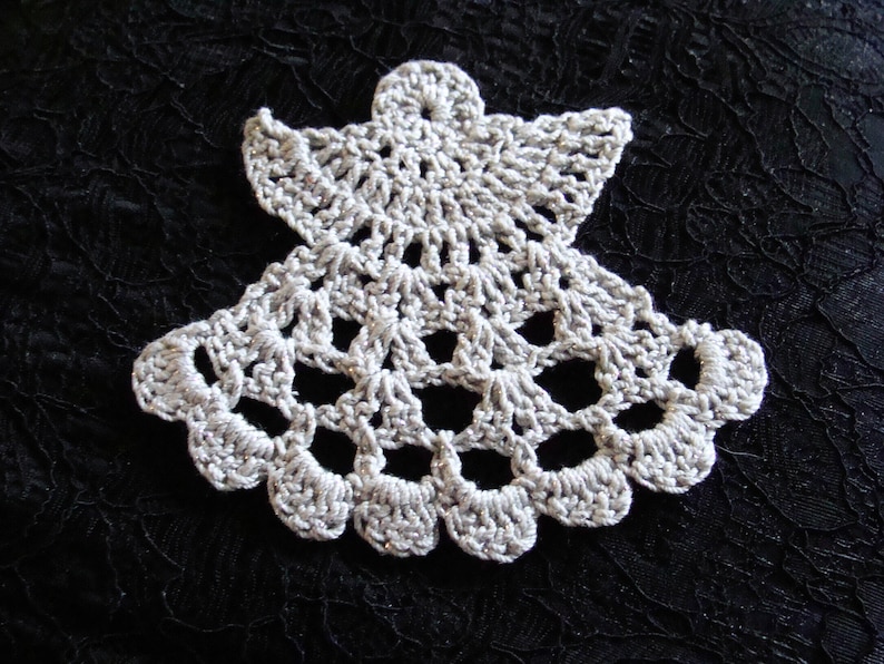 Puede incluir: Un adorno de &aacute;ngel de crochet blanco con un dise&ntilde;o delicado. El adorno est&aacute; hecho de hilo fino y tiene un aspecto de encaje.