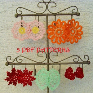 Op de afbeelding: Vijf paar gehaakte oorbellen getoond op een metalen standaard. De oorbellen zijn in verschillende kleuren en ontwerpen, waaronder roze, oranje, rood en groen. De tekst "5 PDF PATTERNS" is zichtbaar op de standaard.