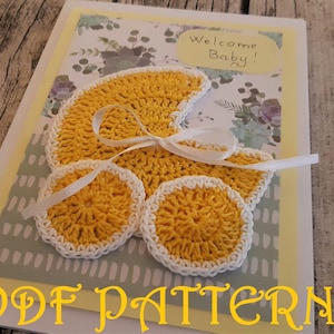 May include: A yellow crocheted baby carriage with a white ribbon and two smaller yellow crocheted circles. The card says "Welcome Baby!" and has a green and white patterned background. The text "PDF PATTERN" is written in yellow at the bottom of the card.