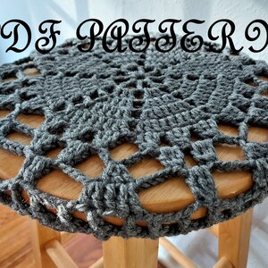 Può includere: Copri sgabello in crochet grigio con un design a pizzo. La copertura è su uno sgabello in legno.
