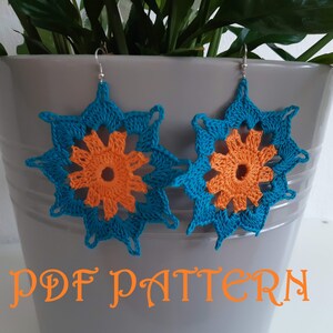 May include: A pair of crocheted earrings with a blue and orange starburst design. The earrings are hanging from a gray surface with the text "PDF PATTERN" below them.