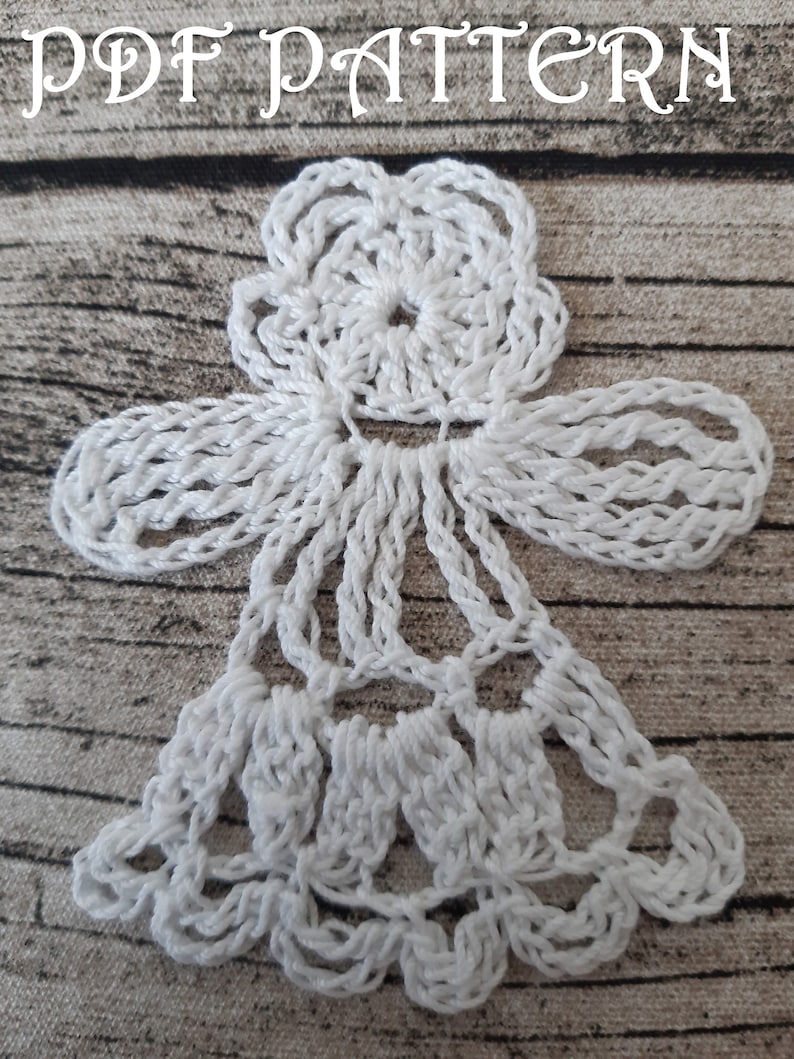 Puede incluir: Adorno de &aacute;ngel blanco tejido a crochet con un dise&ntilde;o de flor en la parte superior y una falda en forma de campana. El adorno est&aacute; sobre un fondo marr&oacute;n texturizado.